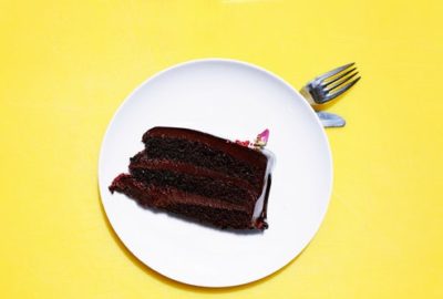 Thick slice of chocolate cake on a white plate on a yellow table