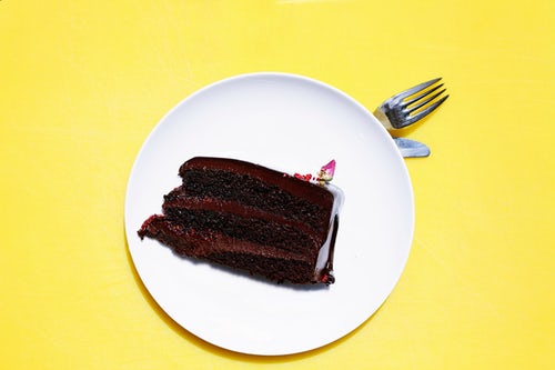 Thick slice of chocolate cake on a white plate on a yellow table