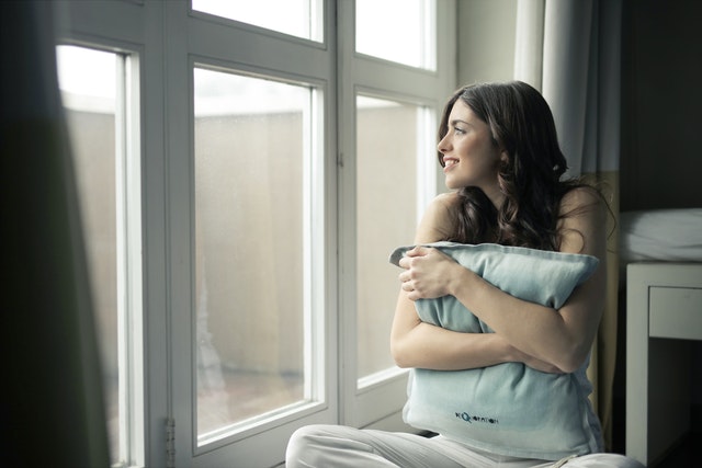 lady looking out window while hugging pillow